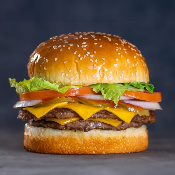 A double cheeseburger with lettuce, tomato, onion, and pickles on a sesame seed bun.