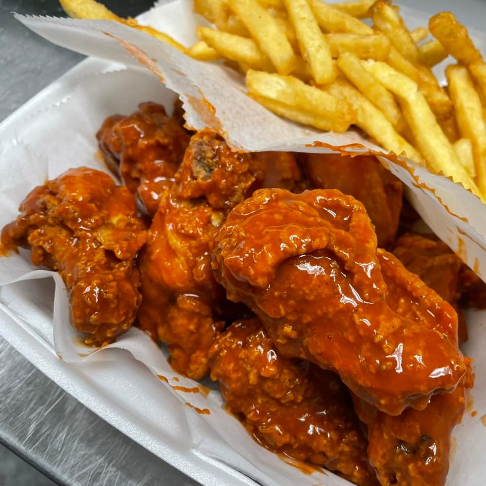 Spicy fried chicken wings and golden french fries in a white takeout container from The Big Catch & Crispy.